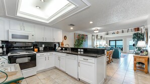 Una cocina moderna con armarios blancos, horno empotrado y zona de comedor con mesa y sillas.