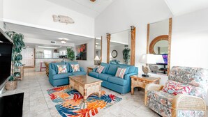 Un salón amplio con un sofá azul, un sillón estampado, una mesa de centro y un televisor.
