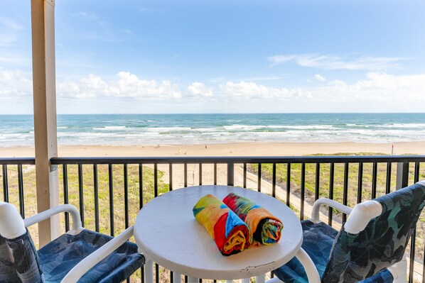 A balcony with a table and chairs overlooking a beach.