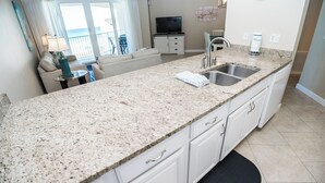 A kitchen with granite countertops, white cabinets, a double sink, and a view of the ocean through large windows. - E604 Amazing Gulf View, 3 Pools, 2 FREE Beach Chairs! (Panama City Beach)