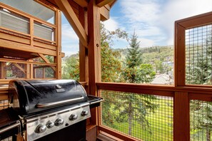 A balcony with a grill, wooden railings, and a view of a forested area.