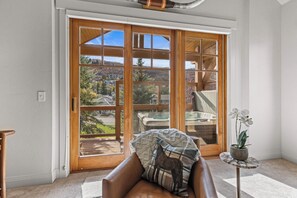 A room with a large sliding glass door leading to a balcony with a view of a residential area and a pool.