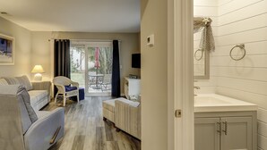 Habitación de hotel con cama, una silla, una mesita, televisión y baño con lavamanos y espejo.