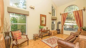 Amplia sala de estar con ventanas grandes, piso de madera, sofá de cuero, alfombra estampada y una mesita con objetos decorativos.