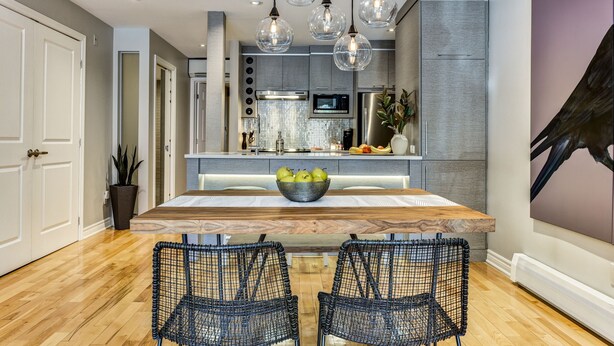 A modern kitchen with a wooden island, black wire chairs, and hanging glass pendant lights. - Modern Montreal Village Condo – Chic Design, Prime Location, Incredible Style! (Centre-Sud South)