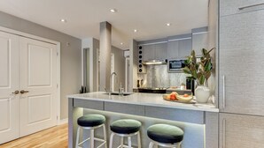 A modern kitchen with a central island, bar stools, and a built-in oven. - Modern Montreal Village Condo – Chic Design, Prime Location, Incredible Style! (Centre-Sud South)