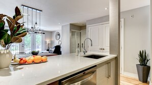 A modern kitchen with a large island, stainless steel appliances, and a view of the outdoors. - Modern Montreal Village Condo – Chic Design, Prime Location, Incredible Style! (Centre-Sud South)