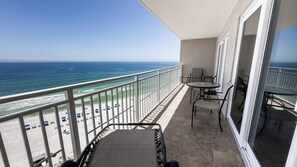 A balcony with a view of the ocean, a table, chairs, and a small rug.