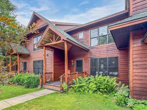 A two-story wooden cabin with a covered porch and a landscaped front yard.