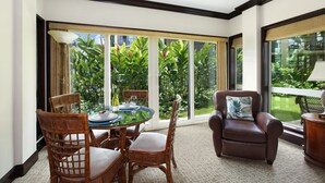 A room with a glass table, wicker chairs, a leather sofa, and large windows overlooking a garden. - Waipouli Beach Resort Beautiful Luxury Garden View (Kapaa)