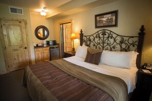 A hotel room with a bed, a desk with a lamp, a microwave, and a door.