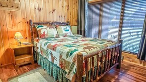 A wooden-paneled bedroom with a bed, a nightstand, a lamp, and a window with blinds.