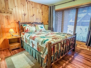 A wooden-paneled bedroom with a bed, nightstand, and window with blinds.