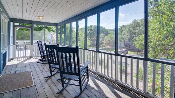 A covered porch with wooden flooring, a railing, and a view of trees and a road. - 12 42nd Avenue by AvantStay | 2 Mins To The Beach | Screened In Porch! (Isle of Palms)