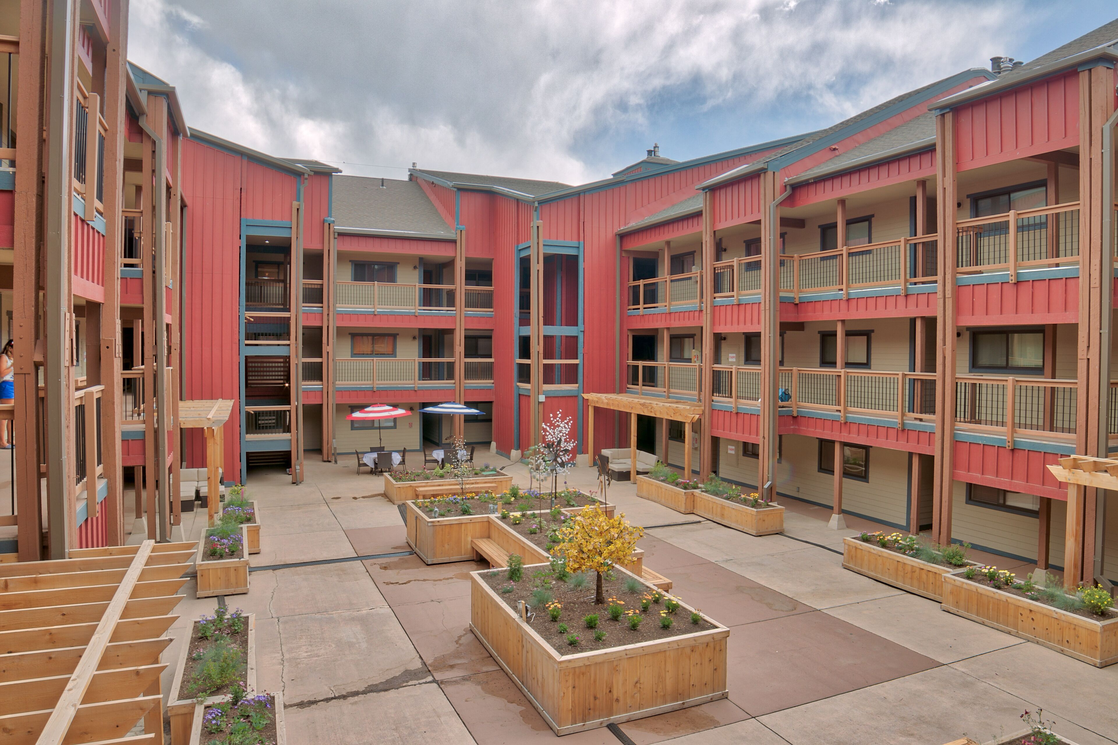 A courtyard with multiple wooden planters, outdoor seating, and a covered area.
