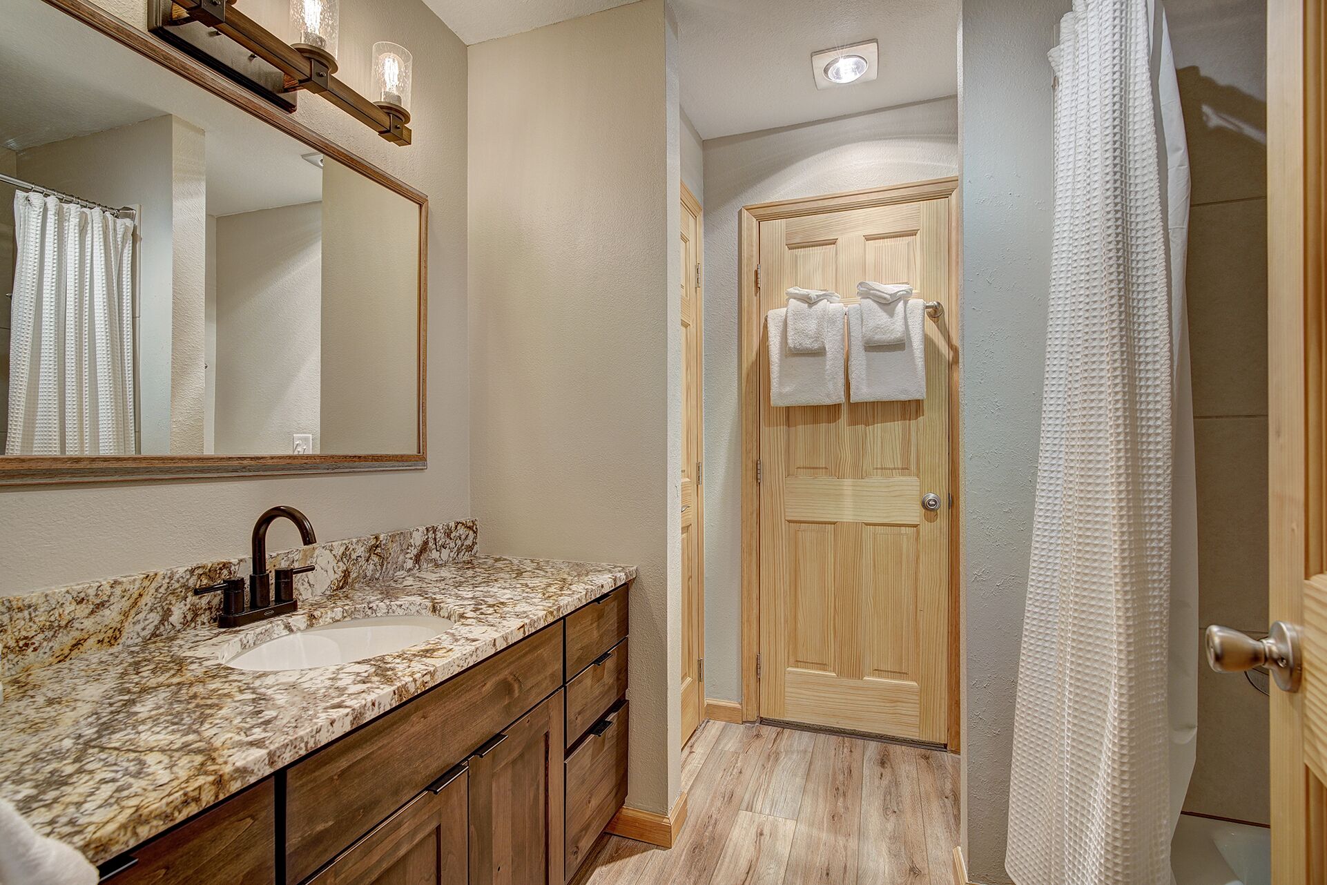 A bathroom with a marble sink, wooden cabinets, a wooden door, and a shower curtain.
