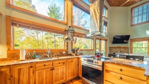 A kitchen with wooden cabinets, a stove, and large windows overlooking a forest. - Beautiful Home, Views, Near Whiteface, Lake Placid (Wilmington)