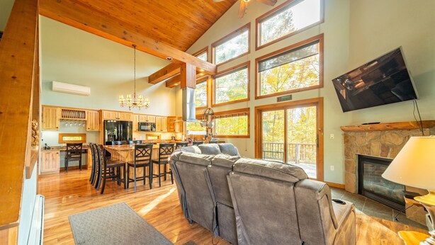 A spacious living area with a large gray sectional sofa, wooden flooring, a fireplace, and a television mounted on the wall. - Beautiful Home, Views, Near Whiteface, Lake Placid (Wilmington)