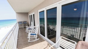 A balcony with white chairs and a table, overlooking a beach and the ocean.