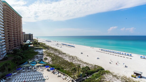 A beach resort with a large building, multiple beach umbrellas, and lounge chairs.