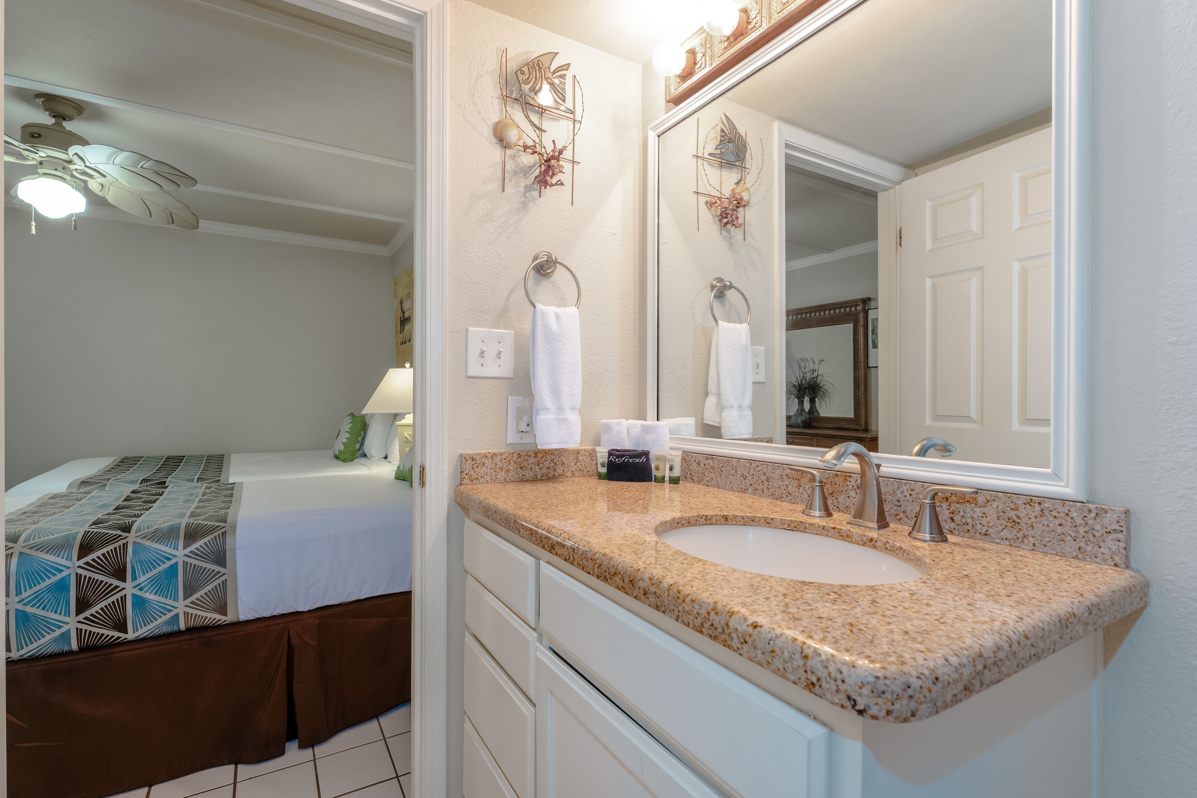 A bathroom with a granite countertop sink, a large mirror, and a ceiling fan.