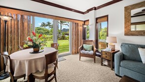 A spacious room with a dining table, a sofa, and a chair. There is a large window with a view of greenery and a mountain. - Waipouli Beach Resort Exquisite Luxury Garden View Large Yard Perfect for Fam (Kapaa)