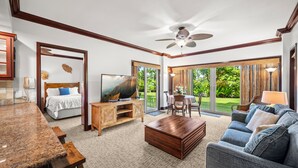 A spacious living room with a large bed, a television, a coffee table, a sofa, and a dining area with a view of the garden. - Waipouli Beach Resort Exquisite Luxury Garden View Large Yard Perfect for Fam (Kapaa)