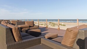A beachside outdoor seating area with wicker furniture and a wooden deck overlooking the ocean.