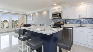 A modern kitchen with white cabinets, a central island with bar stools, a microwave, and a dishwasher.