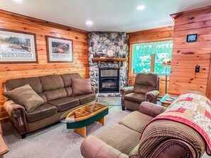 A cozy cabin interior with a stone fireplace, wooden walls, and a sofa set.