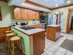 A kitchen with wooden cabinets, a central island with stools, and a refrigerator.