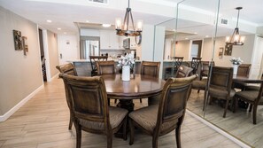 A dining area with a round table surrounded by chairs, a chandelier, and a large mirror reflecting the room.