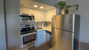 A modern kitchen with white cabinets, stainless steel appliances including a refrigerator, oven, and microwave, and a tiled backsplash.