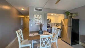 A compact kitchen with white cabinets, a stainless steel refrigerator, and a dining table with chairs.