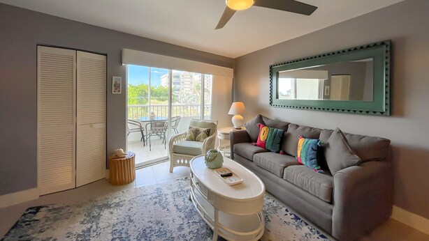 A living room with a ceiling fan, a sofa with colorful pillows, a coffee table, a lamp, and a large mirror on the wall.