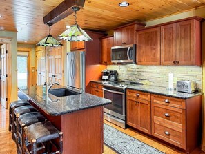 A kitchen with wooden cabinets, a granite countertop, stainless steel appliances, and a bar area with stools.