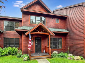 A two-story wooden house with a porch, a flag, and a well-maintained lawn.