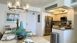 A modern kitchen with a stainless steel refrigerator, a microwave, and a ceiling fan. There is a dining area with a table set for two, featuring a decorative centerpiece. - South Seas T3-1509: Beautifully Updated Condo;  What a View! (Marco Island)