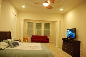 A bedroom with a bed, a red sofa, a TV on a dresser, and a ceiling fan. - Spacious 5BR House, 2 pools & pickle ball, bike to beach, linen provided (Rehoboth Beach)