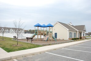 A playground with a slide and climbing structures, a bench, and a building with a porch. - Spacious 5BR House, 2 pools & pickle ball, bike to beach, linen provided (Rehoboth Beach)