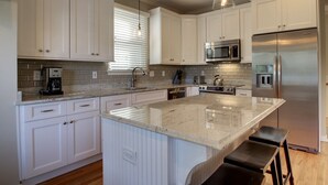 A modern kitchen with white cabinetry, a large island, stainless steel appliances, and pendant lighting. - 73 Grand Pavilion by AvantStay | Corner Lot, Porch (Isle Of Palms)
