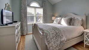 A bedroom with a bed, a dresser, a television, and a window with curtains. - 73 Grand Pavilion by AvantStay | Corner Lot, Porch (Isle Of Palms)