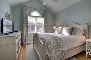 A bedroom with a bed, a dresser, a television, and a window with curtains. - 73 Grand Pavilion by AvantStay | Corner Lot, Porch (Isle Of Palms)