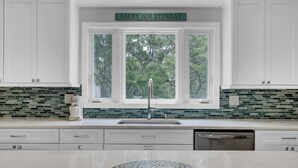 Une cuisine moderne avec des meubles blancs, un pare-feu en carreaux verts et une fenêtre donnant sur les arbres.