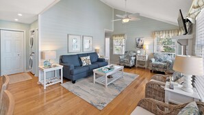 Un salon avec un canapé bleu, une table basse, des fauteuils en osier et un ventilateur de plafond.