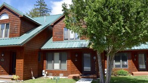 A two-story wooden cabin with a green metal roof, numbered doors, and a 'Reserved' sign in the front yard. - Townhome B4 - 4th Lake (Inlet)