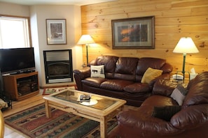 A living room with a leather sofa, a glass coffee table, a fireplace, and two wall-mounted lamps.