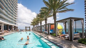 A swimming pool with lounge areas, palm trees, and a view of the ocean. - 38th-floor beachfront residence with panoramic ocean & city views (Hollywood Beach)