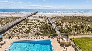 Uitzicht op een strand met een lange pier, een zwembad en ligbedden.