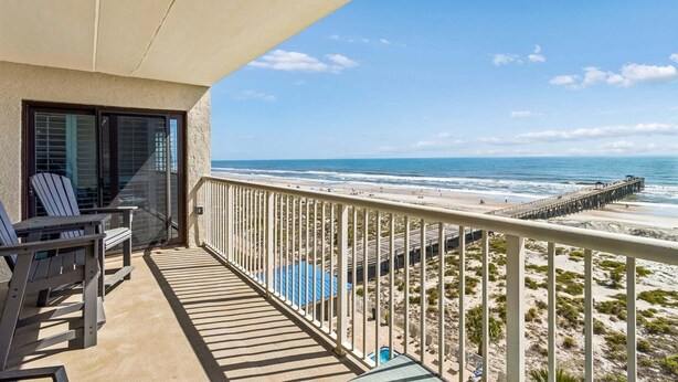 Een balkon met stoelen en uitzicht op het strand en de pier.
